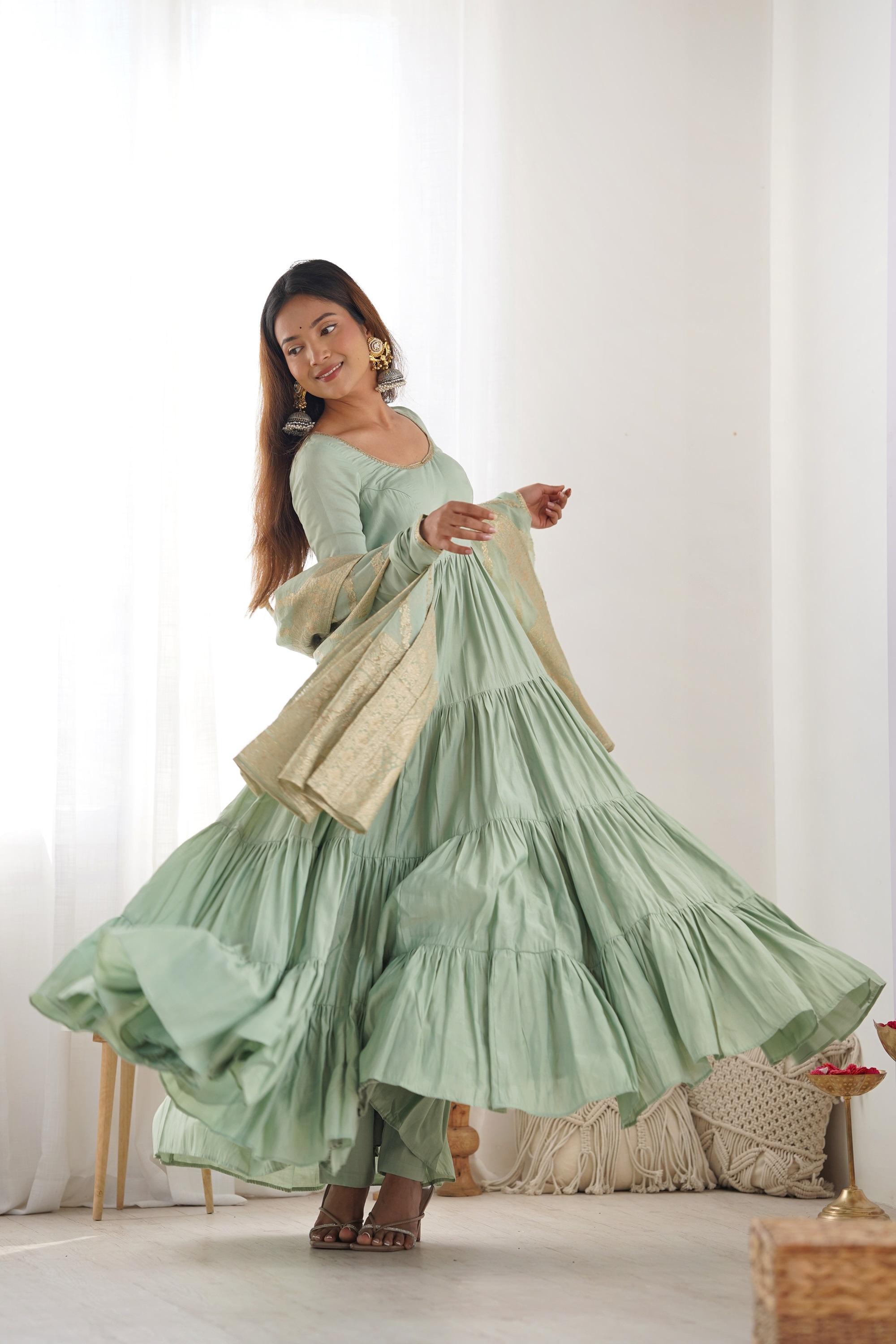 A woman wearing a flowing light green Anarkali suit with a heavy zari woven dupatta